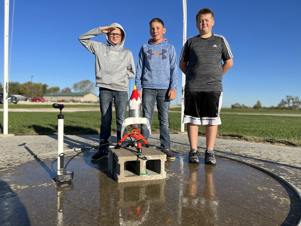 three sixth graders stand ready to launch their soda bottle rocket