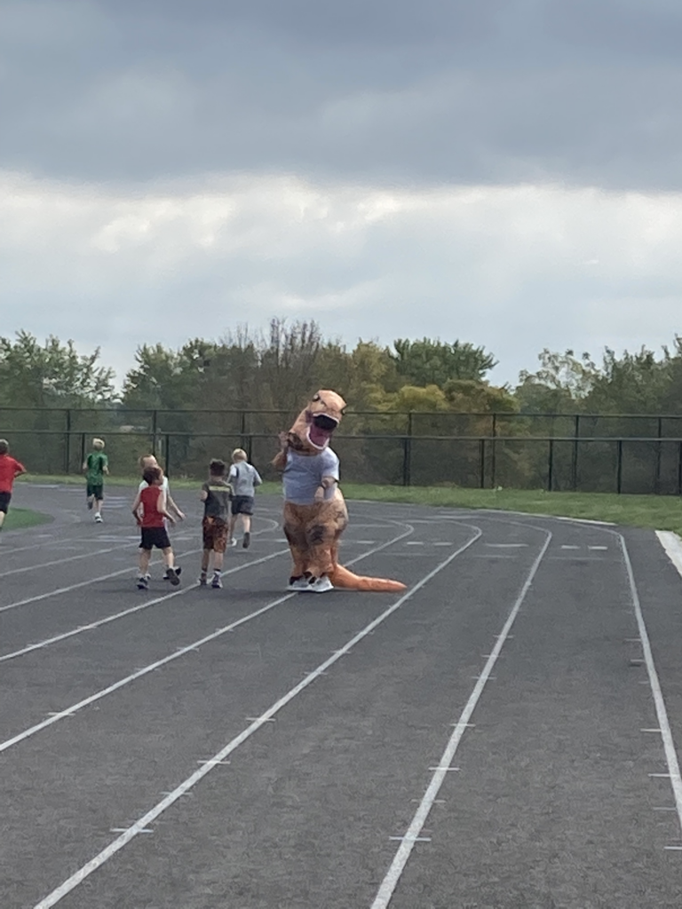 A person in a t-rex costume joins walkers on the track.
