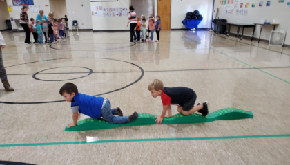 Two preschool students crawl in a line during PE class.