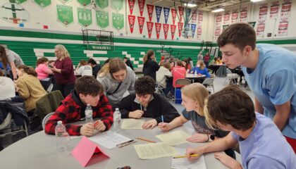 academic team of six high school students works around a round table in a gym to compete in a quiz bowl