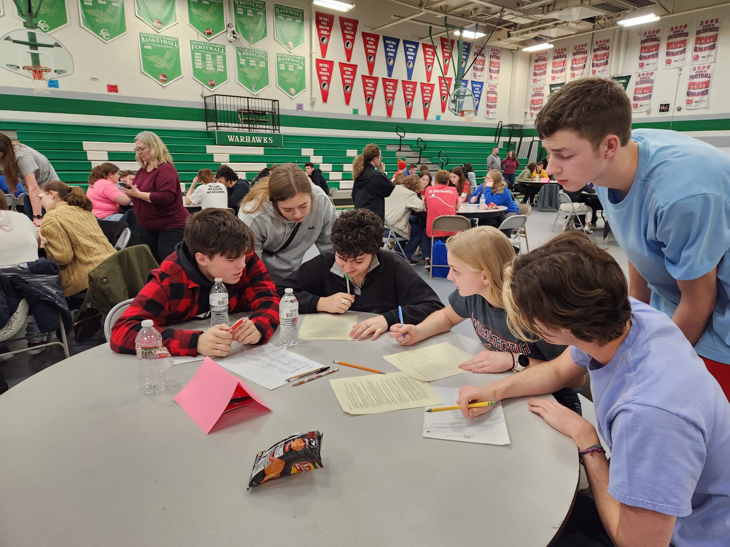 academic team of six high school students works around a round table in a gym to compete in a quiz bowl